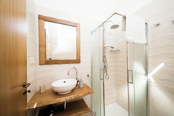 A modern bathroom with a wooden vanity, a white sink, a glass shower enclosure, and a wooden door.