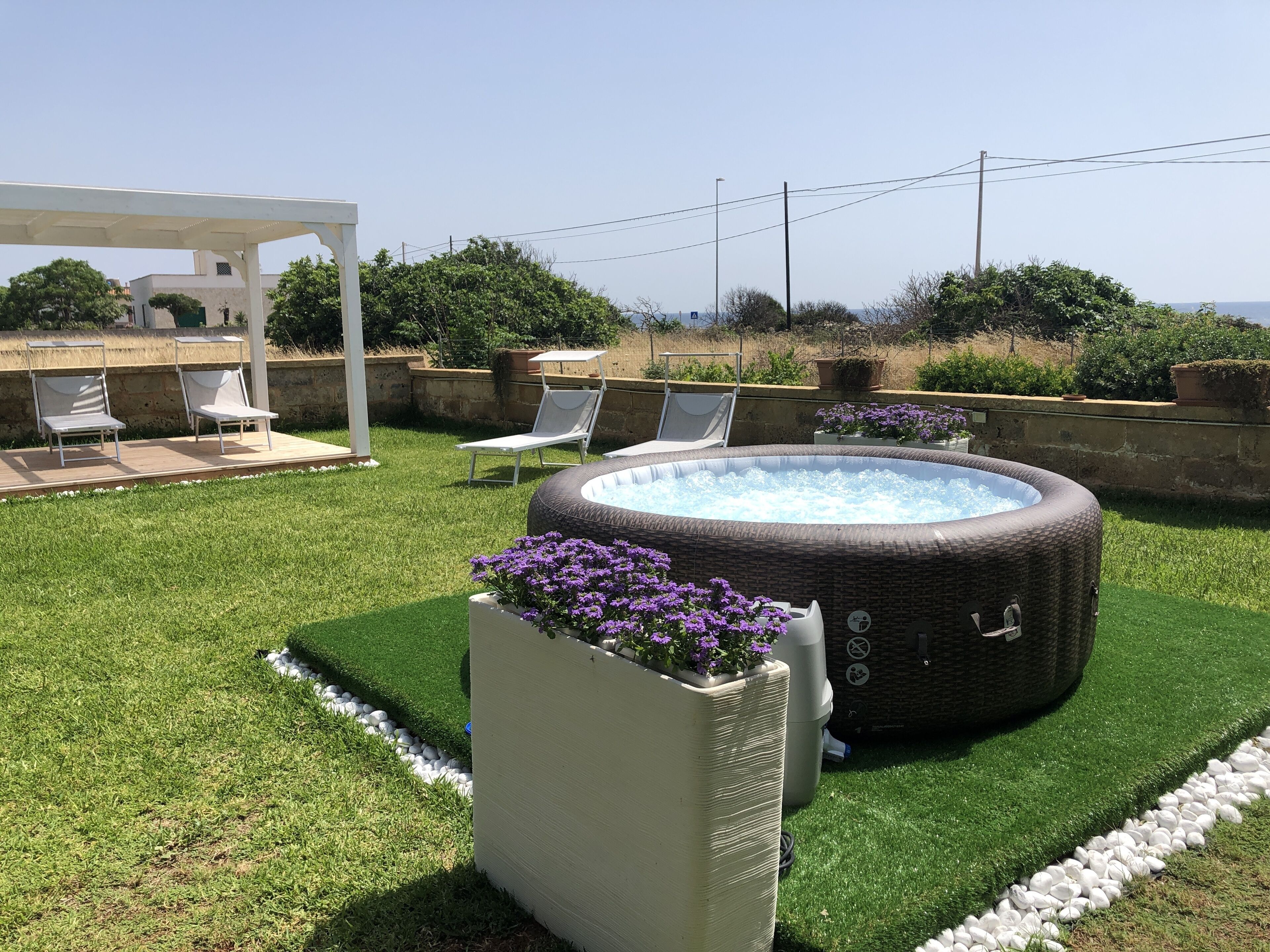 A backyard with a hot tub, lounge chairs, and a pergola.