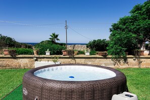 Ein Whirlpool in einem Garten mit einer Steinmauer, Pflanzgefäßen und Blick auf das Meer.