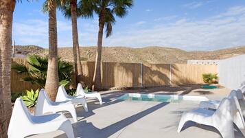 Un jardin avec une piscine, des chaises longues blanches, des palmiers et une clôture en bois.