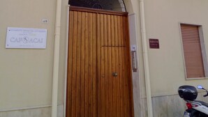 Un edificio con puerta de madera, balcones con barandillas metálicas y un letrero en la pared.