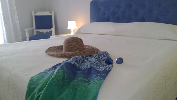 Una cama bien hecha con un cabecero azul, un sombrero estampado y gafas de sol sobre la cama.