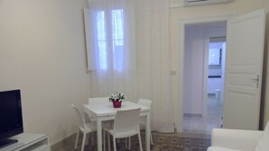 Una habitación pequeña y limpia con una mesa blanca, sillas, un televisor y un suelo con diseño.