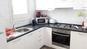 Una cocina moderna con armarios blancos, encimera negra, fregadero, microondas, tostadora, hervidor y cocina a gas.