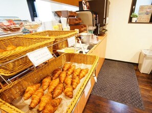 Une vitrine de boulangerie avec des paniers remplis de viennoiseries et une machine à café.