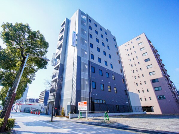 Un bâtiment moderne à plusieurs étages, avec une façade combinant verre et béton, un panneau de signalisation indiquant la présence d’un parking, et un ciel dégagé.