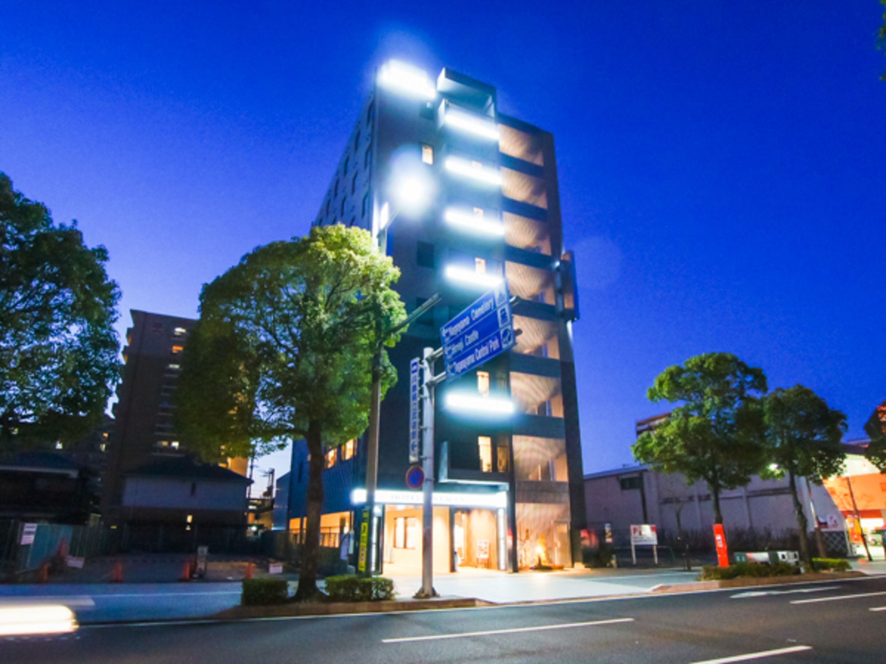A multi-story building with illuminated signage, a street in front, and trees.