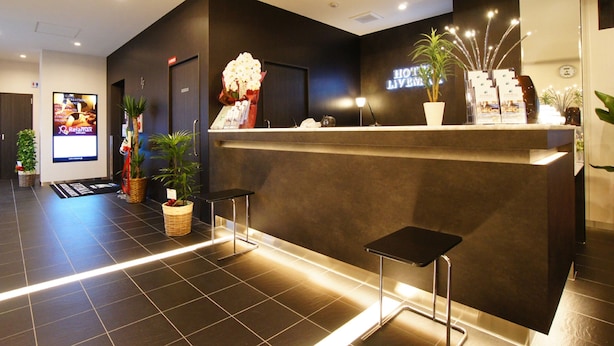 Un espace d’accueil d’hôtel au design moderne, comprenant un comptoir d’accueil, des plantes en pot et un écran numérique affichant des informations sur l’hôtel.
