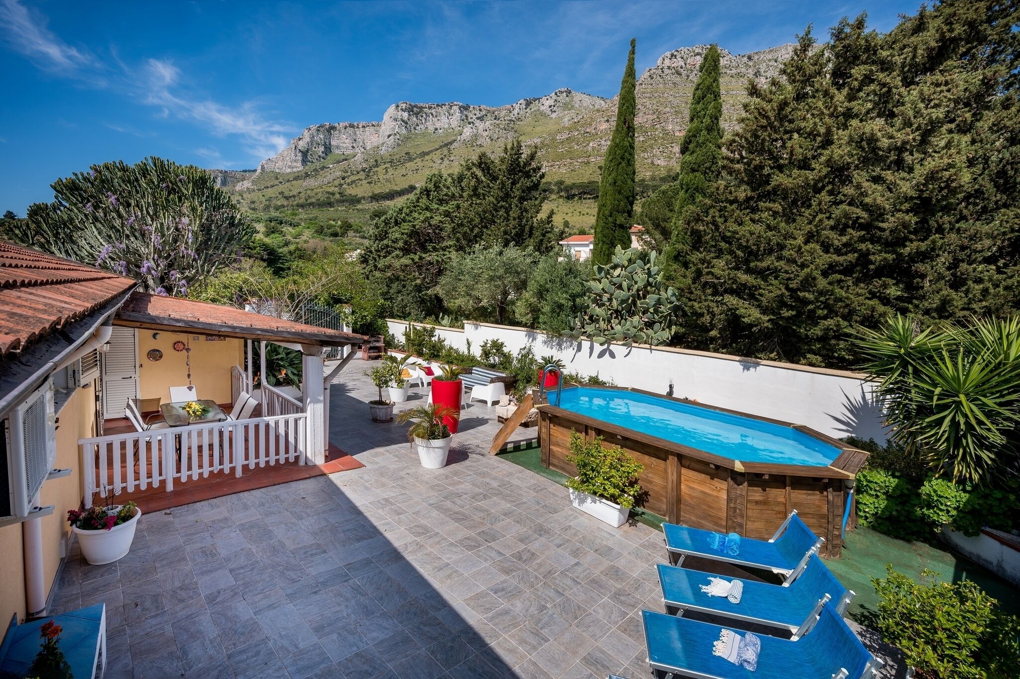 A pool area with a wooden deck, lounge chairs, and a view of mountains.