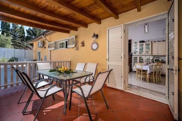 An outdoor patio with a table and chairs, a wooden ceiling, and a view of the kitchen through an open door. - Villa Gagliardetta splendid villa with swimming pool between the greenery and the sea. (Castellammare del Golfo)
