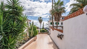 A paved pathway leading to a building with a white wall and decorative metal railing.