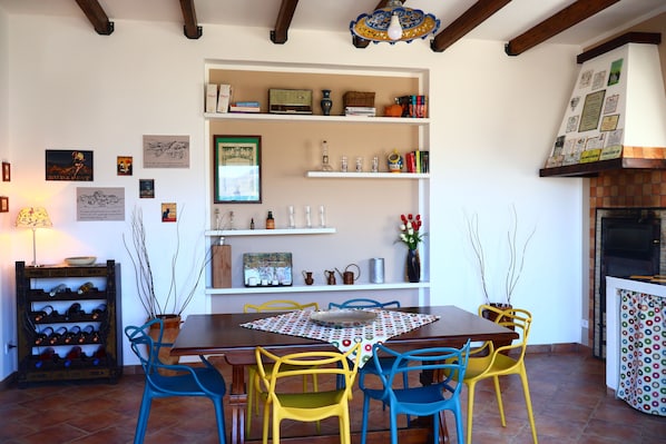 Un comedor con una mesa de madera, sillas coloridas y una estantería para vinos.