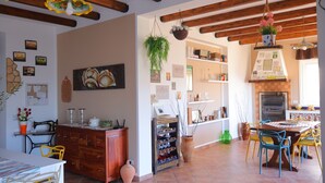 A dining area with a wooden table and chairs, a kitchen with a tiled backsplash, and a hanging plant.