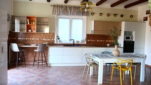 A modern kitchen with white cabinetry, a central island with bar stools, a dining table with chairs, and a hanging light fixture.