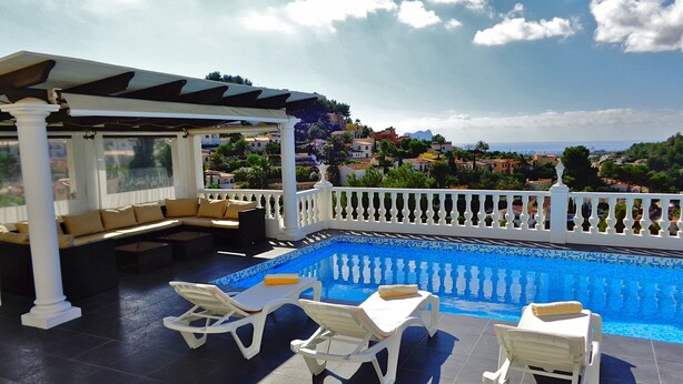 Area piscina sul tetto con poltronde bianche, zona salotto coperta e vista su una cittadina costiera.