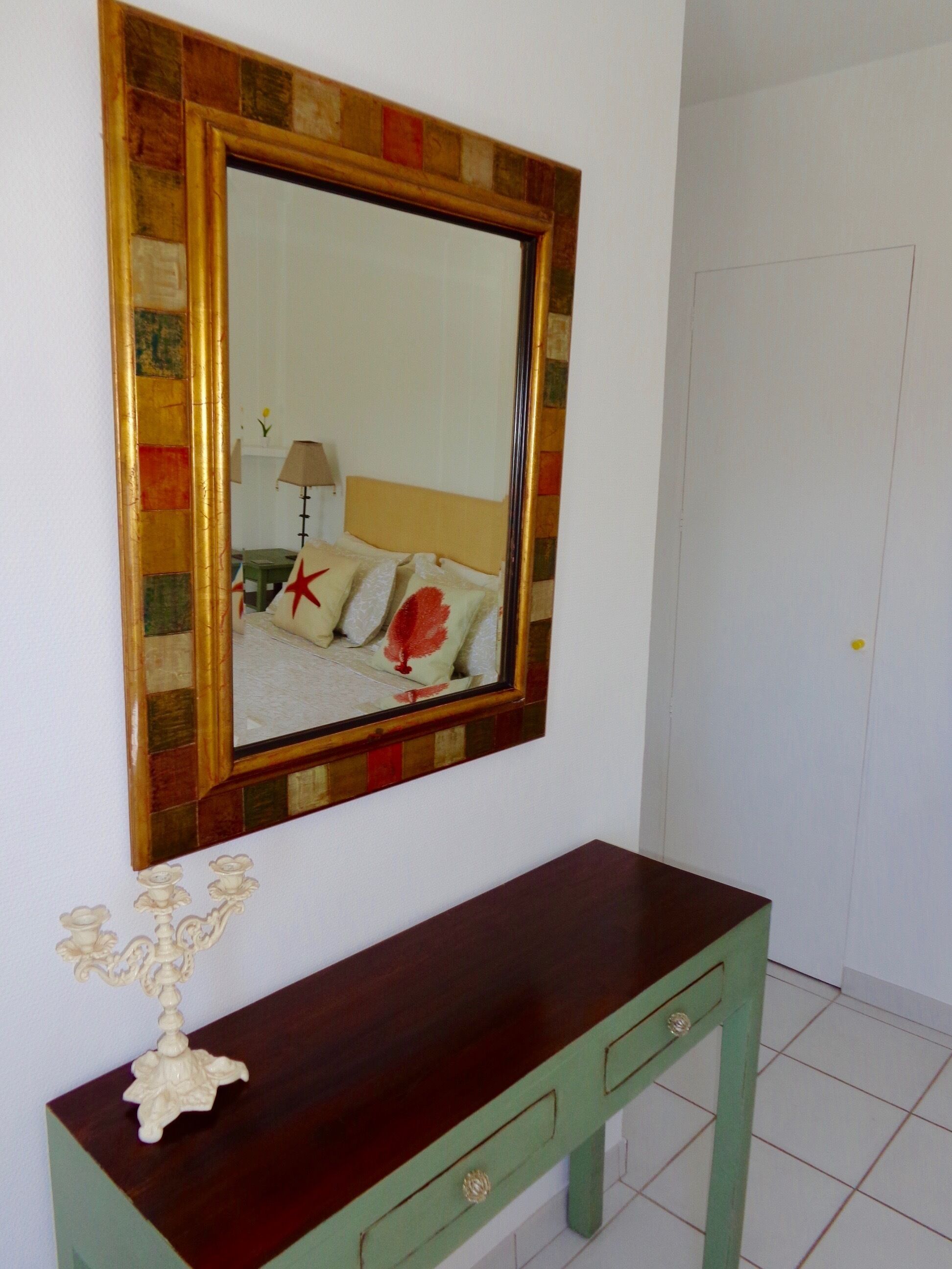 Une pièce avec un grand miroir au mur, une console en bois avec des tiroirs et un lit avec des oreillers et une lampe.
