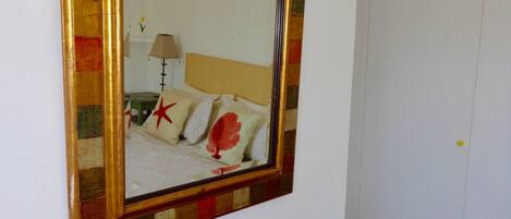 Une pièce avec un grand miroir au mur, une console en bois avec des tiroirs et un lit avec des oreillers et une lampe.