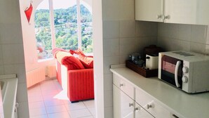Una cucina con mobili bianchi, un forno a microonde e un divano rosso nella zona soggiorno adiacente.