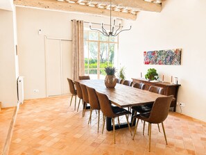 Un coin repas avec une grande table en bois, des chaises marron, un lustre et une fenêtre avec des rideaux.
