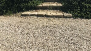 Ein Kiesweg, der zu einer Steintreppe führt, umgeben von dichtem Gebüsch.