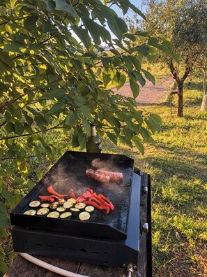 Een draagbare barbecue met worstjes en groenten die buiten worden bereid.