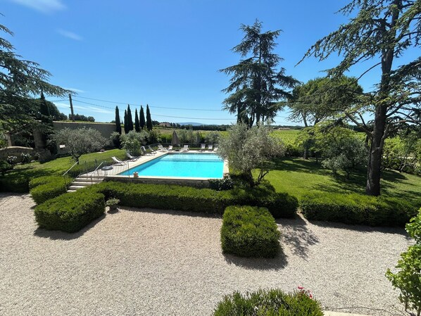 Una piscina rectangular rodeada de setos y árboles cuidados, con un cielo azul despejado.