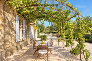 Un bâtiment en pierre doté d’un espace extérieur abrité avec des tables et des chaises, et offrant une vue sur un jardin.
