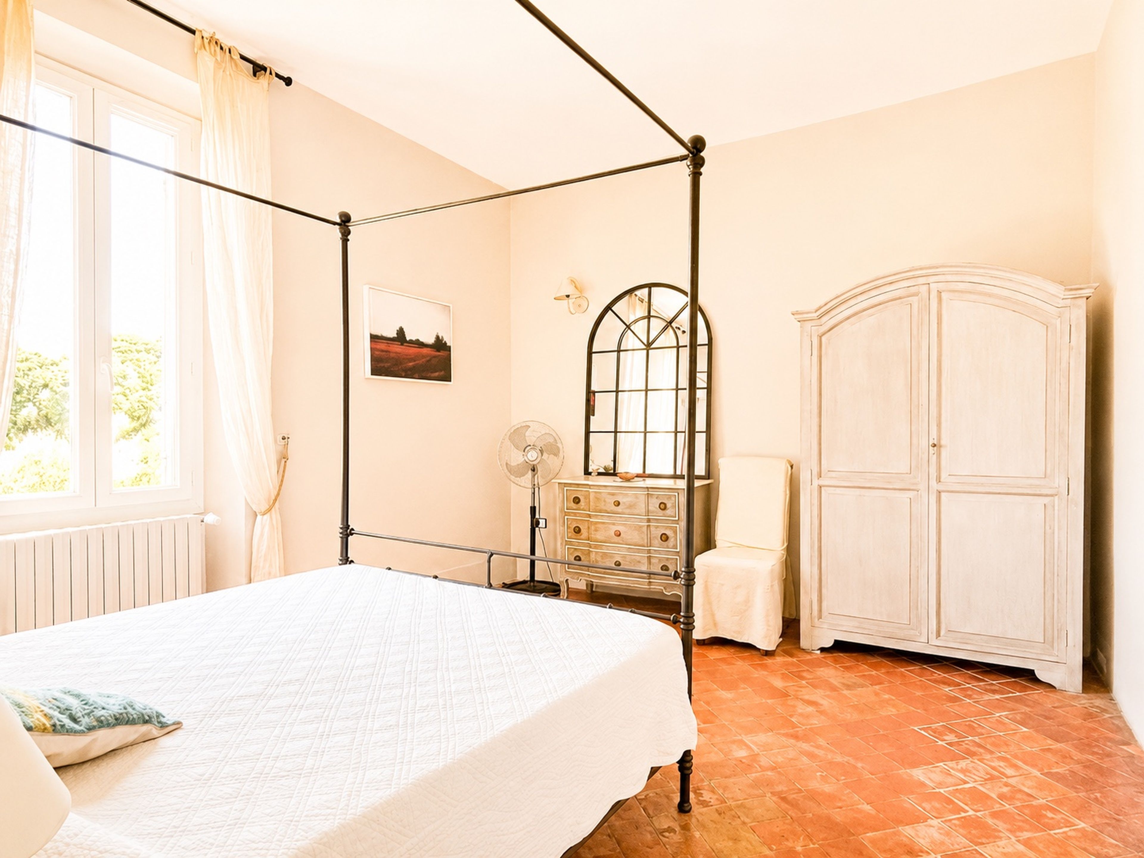 Un dormitorio con cama con dosel, cómoda, espejo y armario.