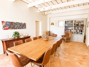 Un comedor espacioso con una larga mesa de madera, sillas tapizadas en tono café, una estantería llena de libros y un gran cuadro abstracto en la pared.