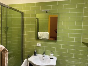 A bathroom with green tiles, a glass shower enclosure, a sink with a mirror, and a towel rack.