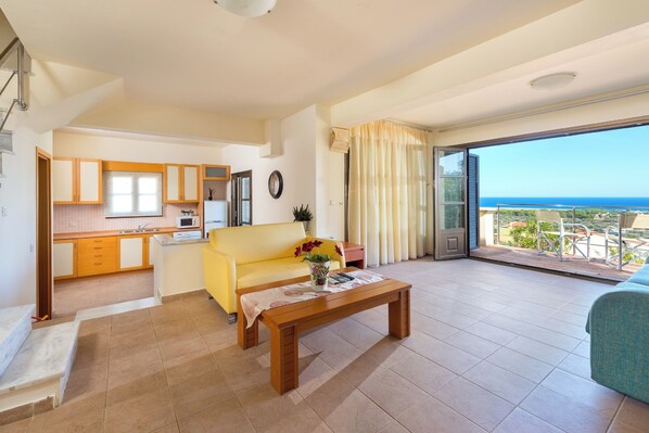 Un vaste espace de vie comprenant un canapé, une table basse en bois et un balcon avec vue sur la mer.