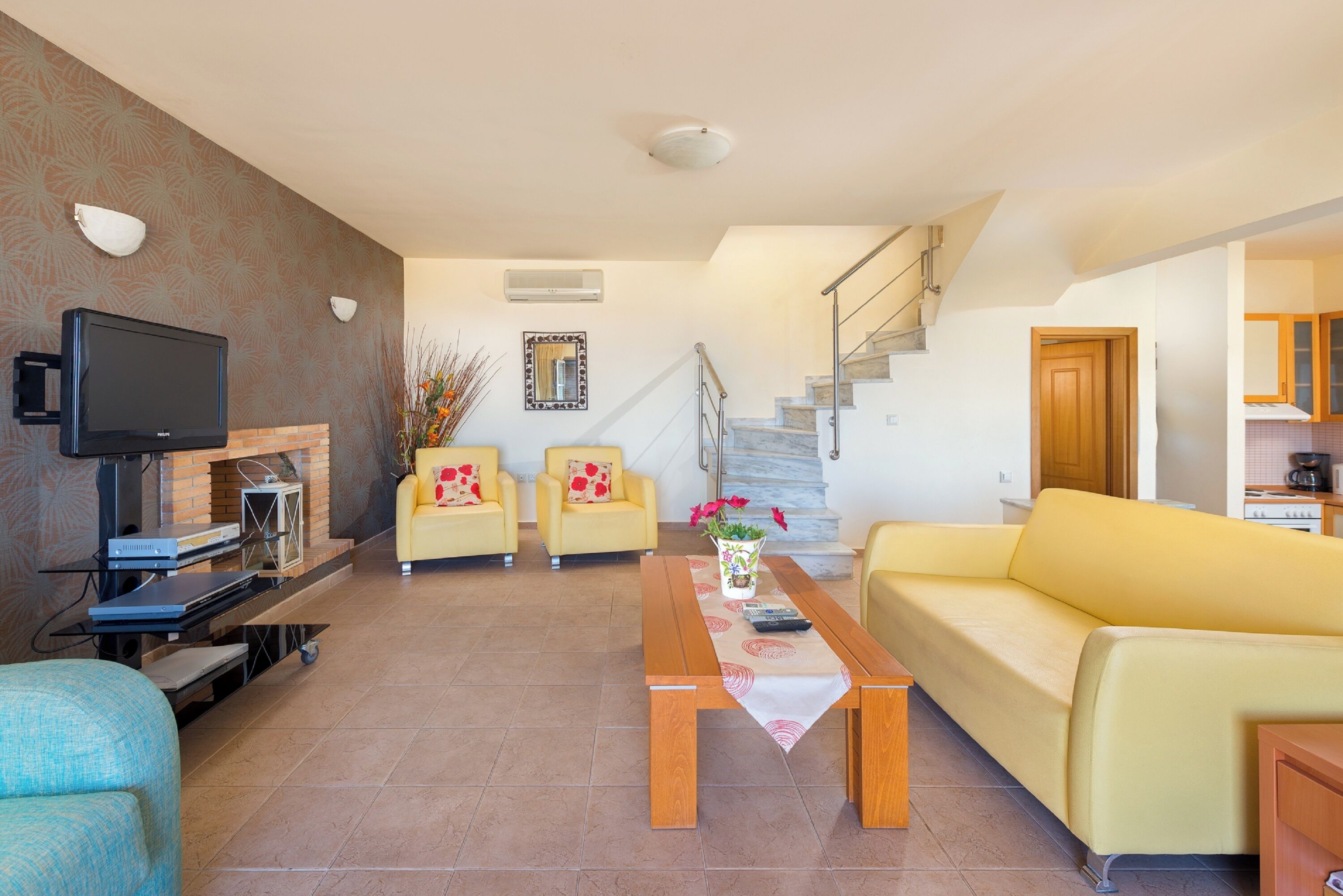 Een woonkamer met een bank, fauteuils, een salontafel, een flatscreen televisie, een open haard en een trap.