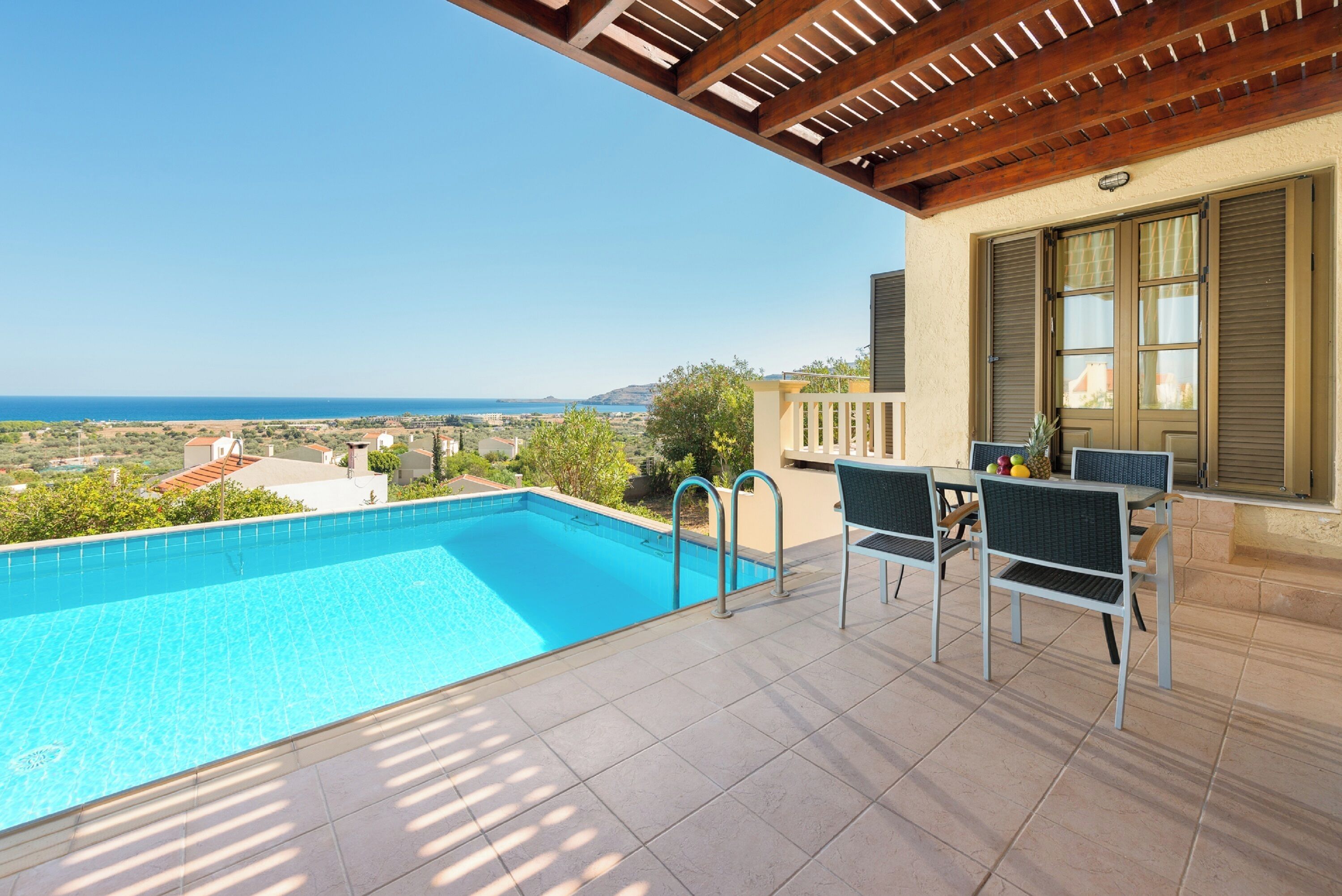 Una piscina con vistas al mar, mobiliario exterior y una pérgola.