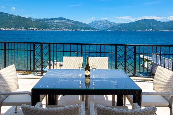 A balcony with a table set for two, overlooking a body of water and mountains.