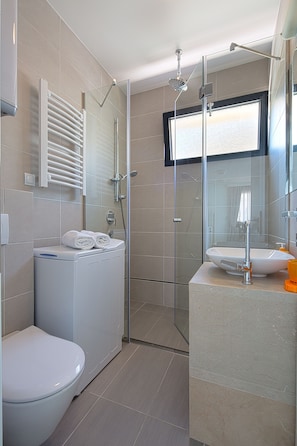 Un baño moderno con inodoro, ducha con mampara de vidrio y lavamanos con espejo.