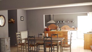 A dining area with a wooden table and chairs, a radiator, and a kitchen in the background. - Paradou quiet house with pool and garden near Les Baux de Provence (Paradou)