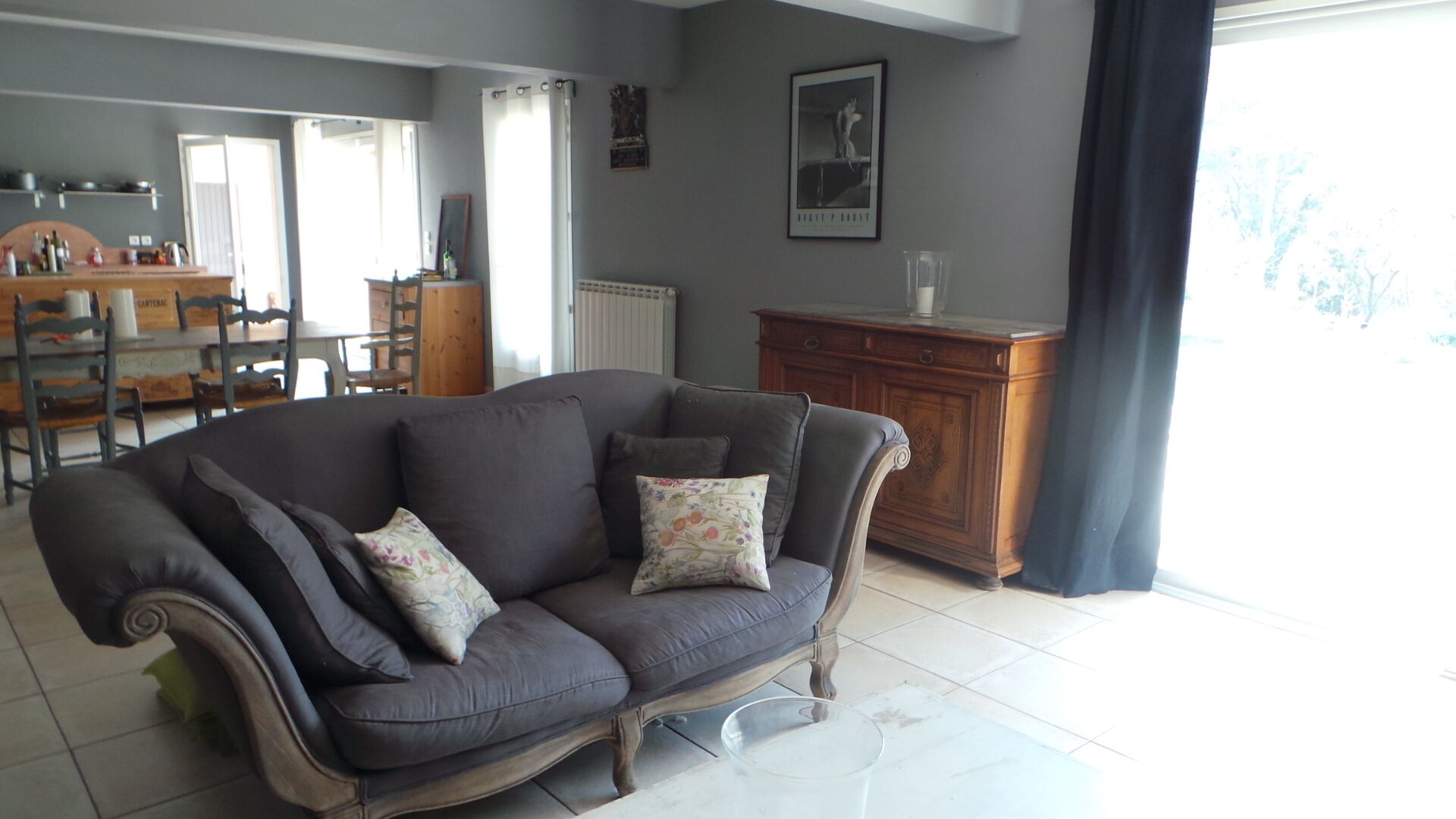A living room with a dark grey sofa, a wooden cabinet, and a dining area in the background.