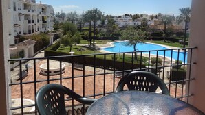 En balkon med udsigt til en swimmingpool, en velholdt have og tilstødende bygninger.