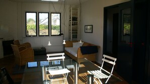 A room with a glass table, wicker furniture, a white sofa, a ladder, and a door. - Nice holiday home for 6 pers., Only 500m from the beach, with own beach cabin (Oostkapelle)