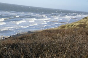 A coastal landscape with waves crashing onto the shore, a grassy embankment, and a wooden fence. - Nice holiday home for 6 pers., Only 500m from the beach, with own beach cabin (Oostkapelle)