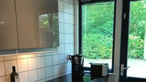 A modern kitchen with a black countertop, white cabinets, a coffee maker, and a window with a view of greenery. - Nice holiday home for 6 pers., Only 500m from the beach, with own beach cabin (Oostkapelle)