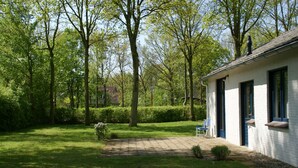 A white building with a paved patio and a blue chair outside. - Nice holiday home for 6 pers., Only 500m from the beach, with own beach cabin (Oostkapelle)