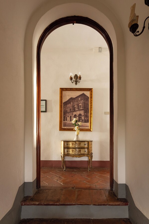 A hallway with a framed picture on the wall, a small table with a vase, and a chandelier.