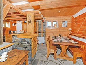 Cozy cabin-style interior with a stone fireplace, wooden dining table, and kitchen area.