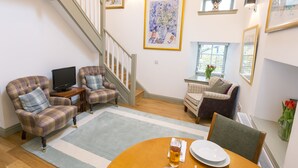Una sala de estar con una escalera, dos sillones, una mesa con un plato y una copa, y un televisor.