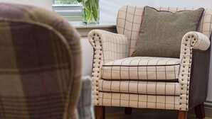 Una sala de estar con un sillón a cuadros, un sofá con un cojín a cuadros y una ventana con persianas.