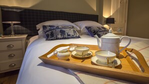 Una cama bien hecha con una bandeja de té, almohadas y una mesita de noche con una lámpara.