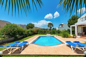 A swimming pool with lounge chairs, surrounded by greenery and buildings. - Apollo Villa located in Kolympia (Kolympia)