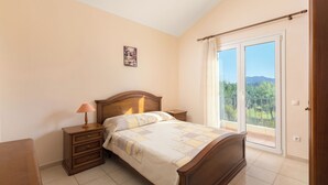 Une chambre à coucher comprenant un lit, des tables de chevet, une commode, une fenêtre avec vue et une porte.