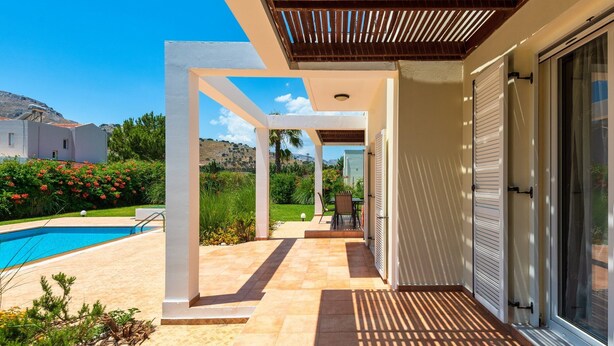 Un espace extérieur abrité comprenant une piscine, une terrasse avec une table et des chaises, et une vue sur une colline.